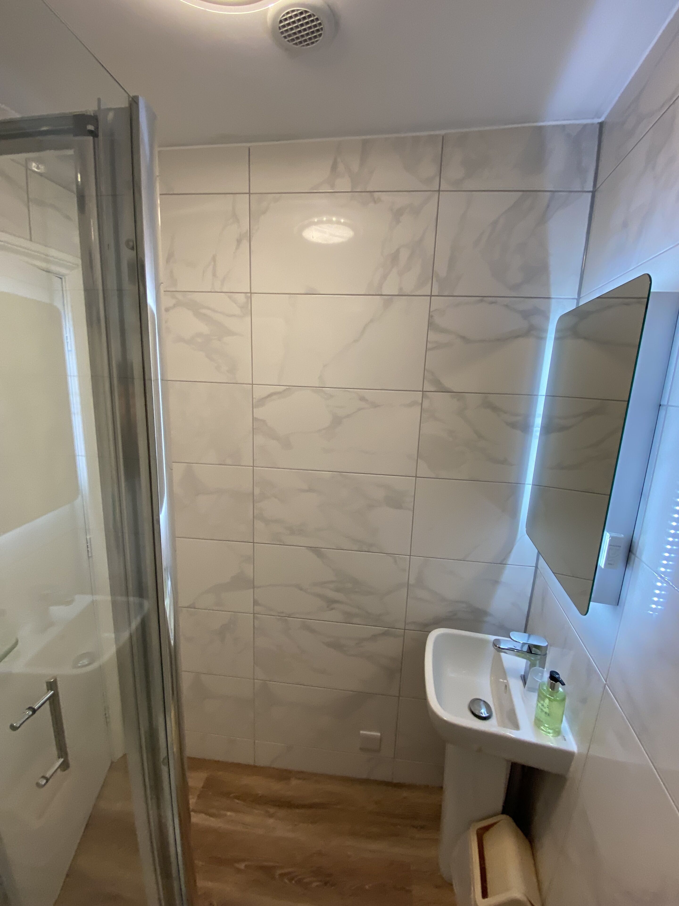 Een badkamer met een glazen douchecabine, een wit wastafelmeubel met een spiegel erboven en marmeren tegels op de muren.