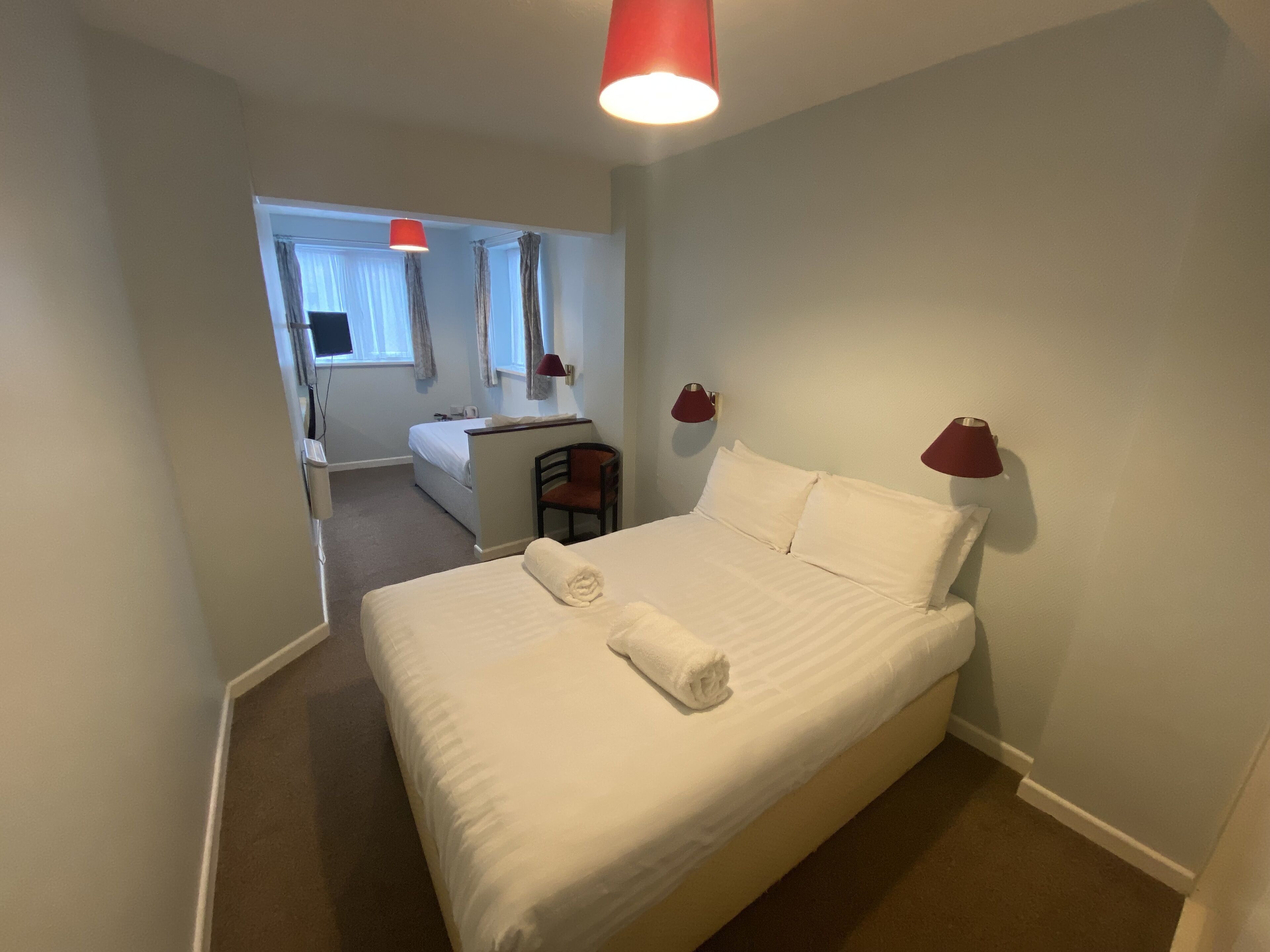 Una habitación de hotel con una cama grande, dos lámparas de noche, una silla, un escritorio y una ventana con cortinas.