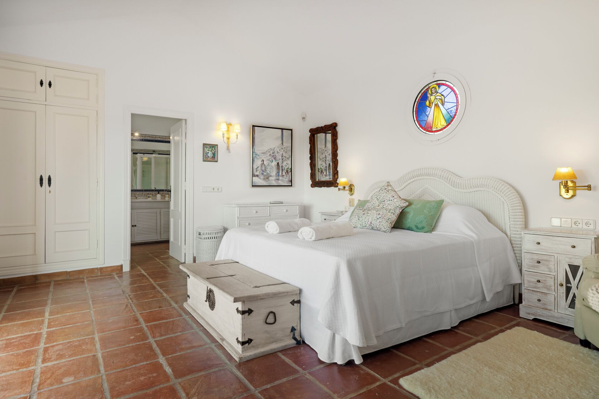 A bedroom with a bed, a chest of drawers, a mirror, and a wall-mounted light fixture.
