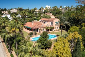 Una casa espaiosa amb piscina, envoltada de vegetació exuberant i palmeres.