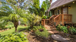 A tropical garden with a wooden staircase leading to a house with a tiled roof. - Mahina Cottage, Mahina Cottage (Maui County)