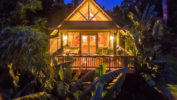 A two-story house with a balcony, surrounded by tropical vegetation. - Mahina Cottage, Mahina Cottage (Maui County)