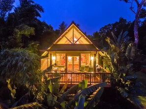 A two-story house with a balcony, surrounded by tropical vegetation. - Mahina Cottage, Mahina Cottage (Maui County)