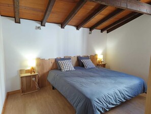 Une chambre avec un plafond en bois, un lit simple recouvert d’une courtepointe bleue, deux lampes de chevet et une petite table de nuit en bois avec une lampe.
