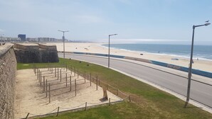 Una carretera costera con una playa a la derecha, un muro de piedra a la izquierda y un cielo despejado.