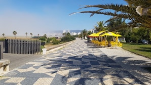 Un sendero pavimentado con sombrillas amarillas y sillas, que conduce a una vista de edificios y palmeras.
