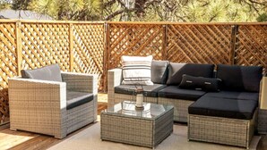 A wicker outdoor seating area with a glass coffee table, cushioned sofas, and a wooden lattice backdrop. - Mountain Retreat w/Foosball/Game Table! Fireplace~Large Deck~Near Park~Dogs OK! (Flagstaff)