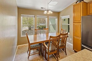 A dining area with a wooden table and chairs, a built-in cabinet, and a view through large windows.