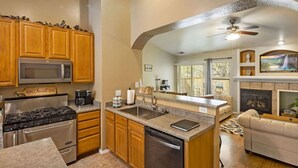 A kitchen with wooden cabinets, stainless steel appliances, a central island, and a fireplace. - Mountain Retreat w/Foosball/Game Table! Fireplace~Large Deck~Near Park~Dogs OK! (Flagstaff)
