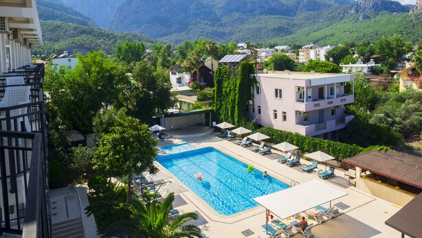 A swimming pool with lounge chairs and umbrellas, surrounded by greenery and buildings, with mountains in the background. - Tal Beach Hotel (Kemer)