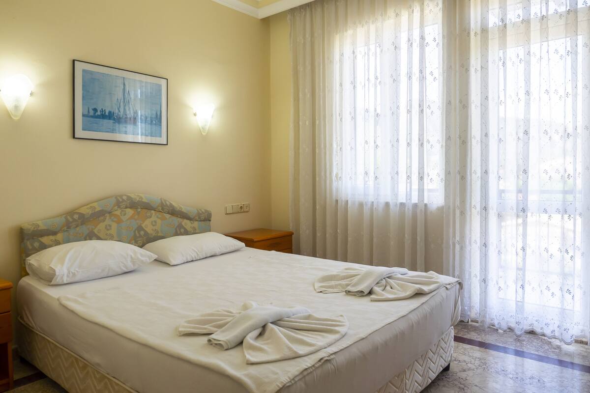 Una cama bien hecha con toallas, un cabecero estampado con motivos florales, una lámpara de pared y un cuadro enmarcado.