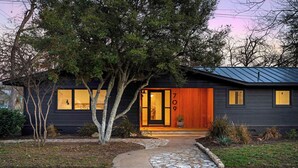 Une maison moderne avec une façade sombre, une porte d’entrée en bois et le numéro 709.