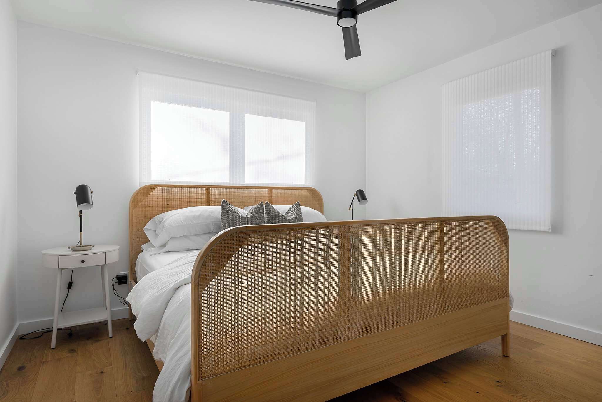 Un dormitorio con cama de madera, paredes blancas y una mesita de noche con lámpara.