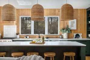 A modern kitchen with a large island, wooden panel walls, and three woven pendant lights. - Hot tub, Game Room, Pet Friendly, Cowboy Pool! (Fredericksburg)