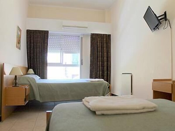 A hotel room with two beds, a desk, a chair, a flat-screen TV mounted on the wall, and an air conditioning unit.
