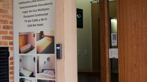 A hotel interior with a bulletin board displaying room types and amenities, a wooden door, and a visible elevator. - Bet Hotel (Buenos Aires)