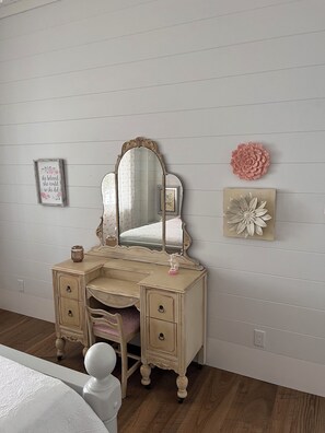 A bedroom with a vanity, a bed, and a dresser.