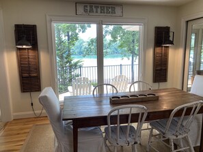 A dining area with a wooden table and white chairs, a sign above the door reading "GATHER", and a view of a lake through the glass door. - Perfect lake property for Clemson Game Day! (Seneca)