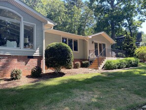 A single-story house with a brick foundation, a covered porch, and a small front yard with a well-maintained lawn and a trimmed bush. - Perfect lake property for Clemson Game Day! (Seneca)