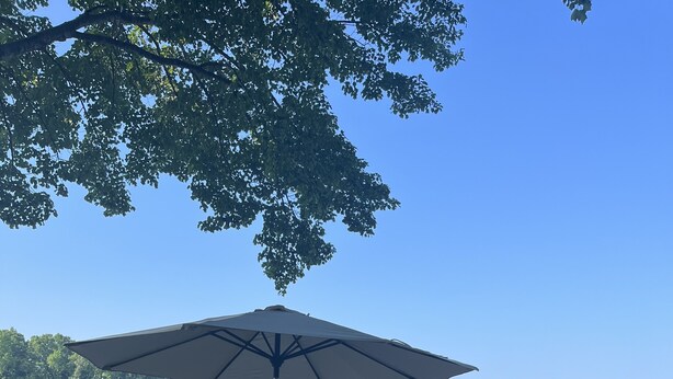 Une terrasse en bois avec des tables de pique-nique et un parasol, donnant sur un lac paisible où sont amarrés des bateaux.