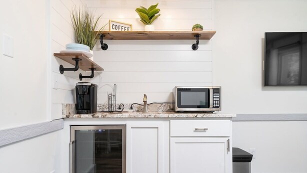 A modern kitchen with white cabinetry, a built-in microwave, a coffee station, and a glass-fronted oven. - DT TC Suite I Queen Bed I Walk Bars + Shops (Traverse City)