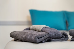 Een netjes opgevouwen set handdoeken op een bed, met een turquoise kussen op de achtergrond.