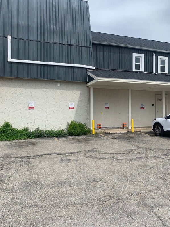 A building with a grey roof and a white facade, featuring a parking area with a white car and bollards.