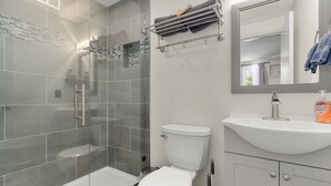 Ein modernes Badezimmer mit Duschkabine aus Glas, einer weißen Toilette und einem Waschbecken mit Spiegel darüber.