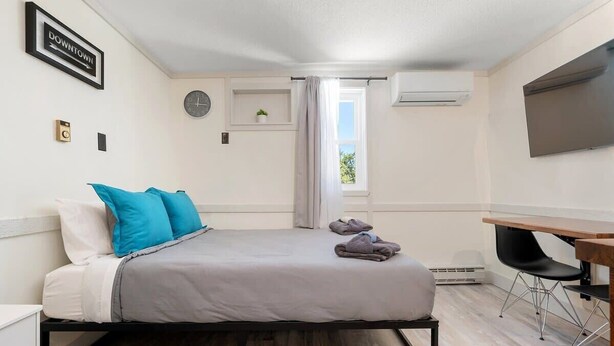 Ein Schlafzimmer mit Bett, Schreibtisch, Stuhl, einer Uhr und einem Fenster.