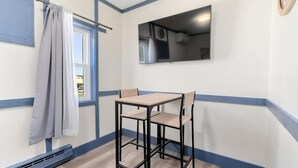 Une petite pièce avec une table et deux chaises, une fenêtre avec des rideaux et un téléviseur à écran plat fixé au mur.