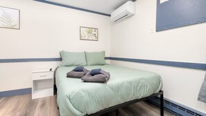 Une chambre à coucher comprenant un lit, une table de chevet, un appareil de climatisation et une horloge murale.