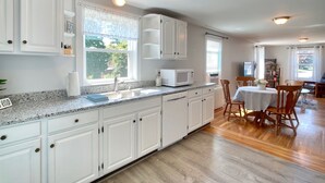 Una cocina moderna con armarios blancos, encimeras de granito y un comedor con sillas y mesa de madera.
