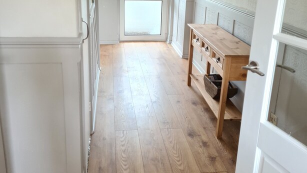 A hallway with wooden flooring, a wooden table with drawers, and a door with frosted glass panels.