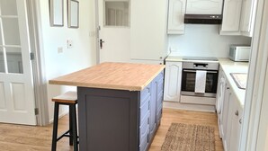 A kitchen with a central island, wooden flooring, white cabinets, and a microwave.
