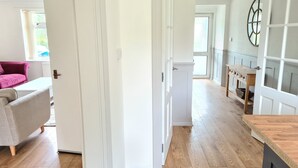 A spacious room with wooden flooring, a white door, and a view of a kitchen area with a wooden table and cabinets.