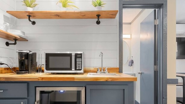 Een kleine keuken met een magnetron, spoelbak en houten planken.