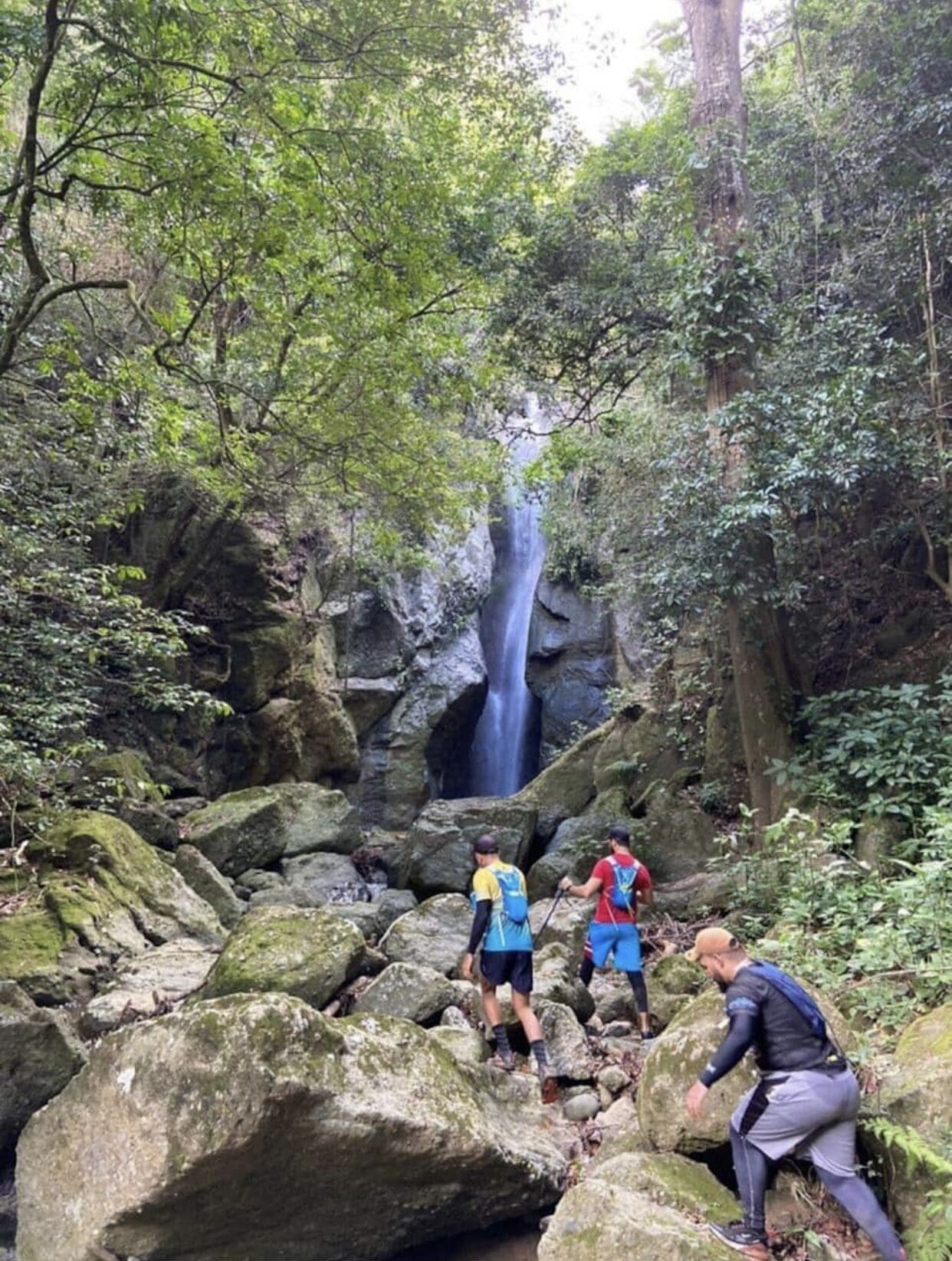 A group of hikers navigating a rocky terrain with a waterfall in the background.