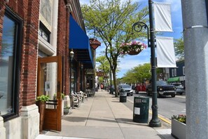 Une vue de rue avec un bâtiment en briques, un auvent bleu, des jardinières suspendues et des voitures garées.