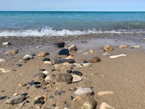 Una spiaggia con ciottoli e rocce sparse sulla sabbia, che si estende fino all'acqua.