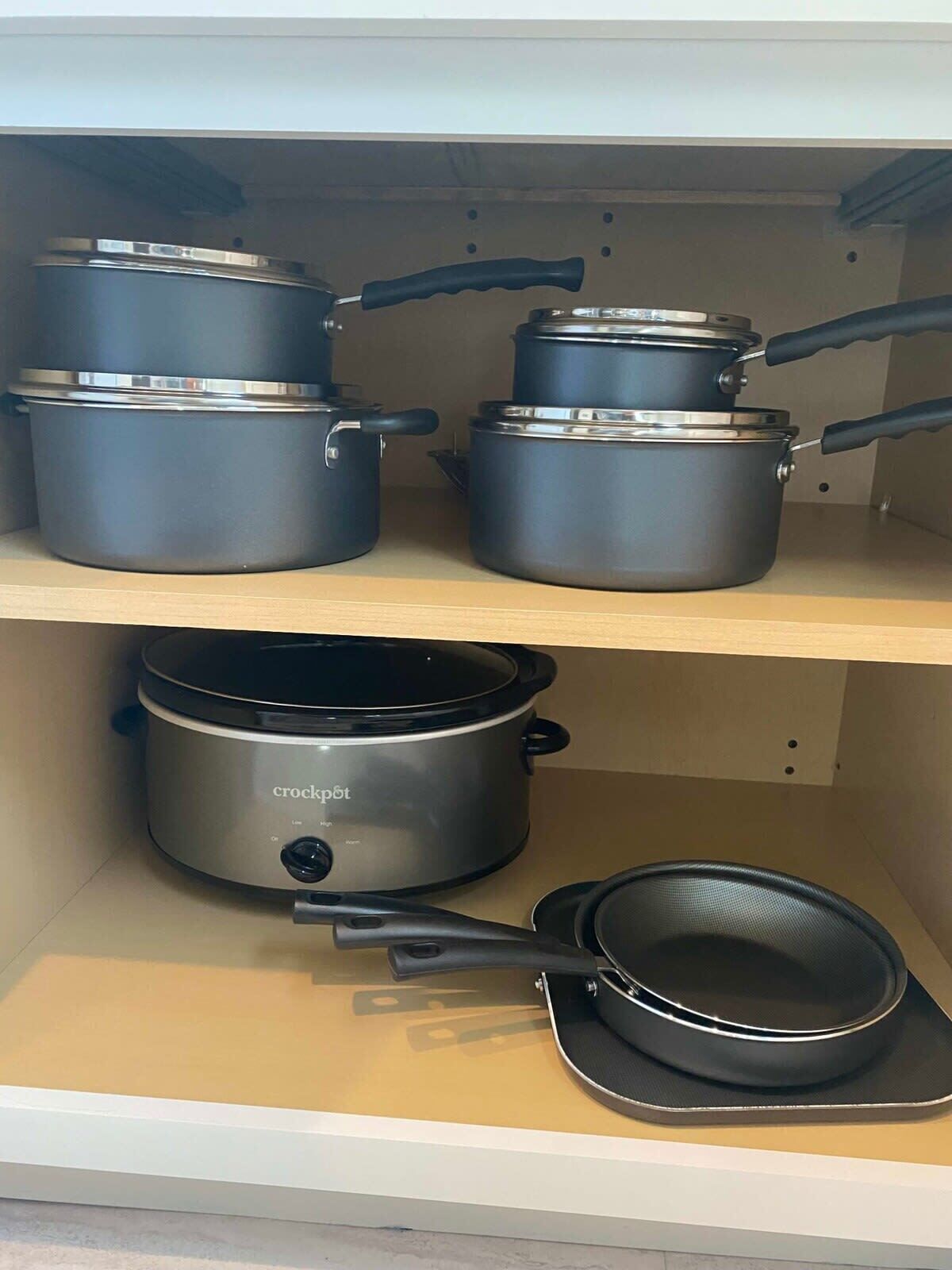 A kitchen shelf with various cookware including pots, pans, and a slow cooker.