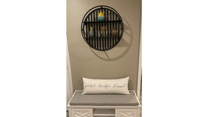 A white bench with a cushion that reads "grateful, thankful, blessed." Above the bench is a circular black shelf with decorative items. - Peak Comfort of Apex (Apex)