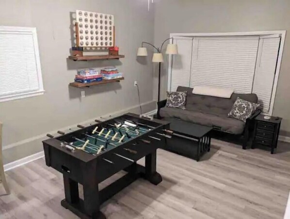 A living room with a foosball table, a sofa, a coffee table, and a lamp.