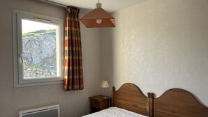 Un dormitorio con cama, mesita de noche, lámpara, ventana con cortinas y radiador.