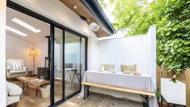 An outdoor patio area with a wooden bench, a table with a white tablecloth, and a white sofa. - Beautiful Home in Heart of Truro (Truro)