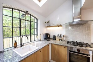 A kitchen with a large window, a gas stove, a built-in oven, and wooden cabinets. - Beautiful Home in Heart of Truro (Truro)