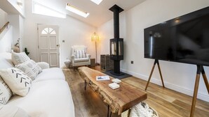A modern living room with a white sofa, a wooden coffee table, a black TV on a stand, a black fireplace, and skylights. - Beautiful Home in Heart of Truro (Truro)
