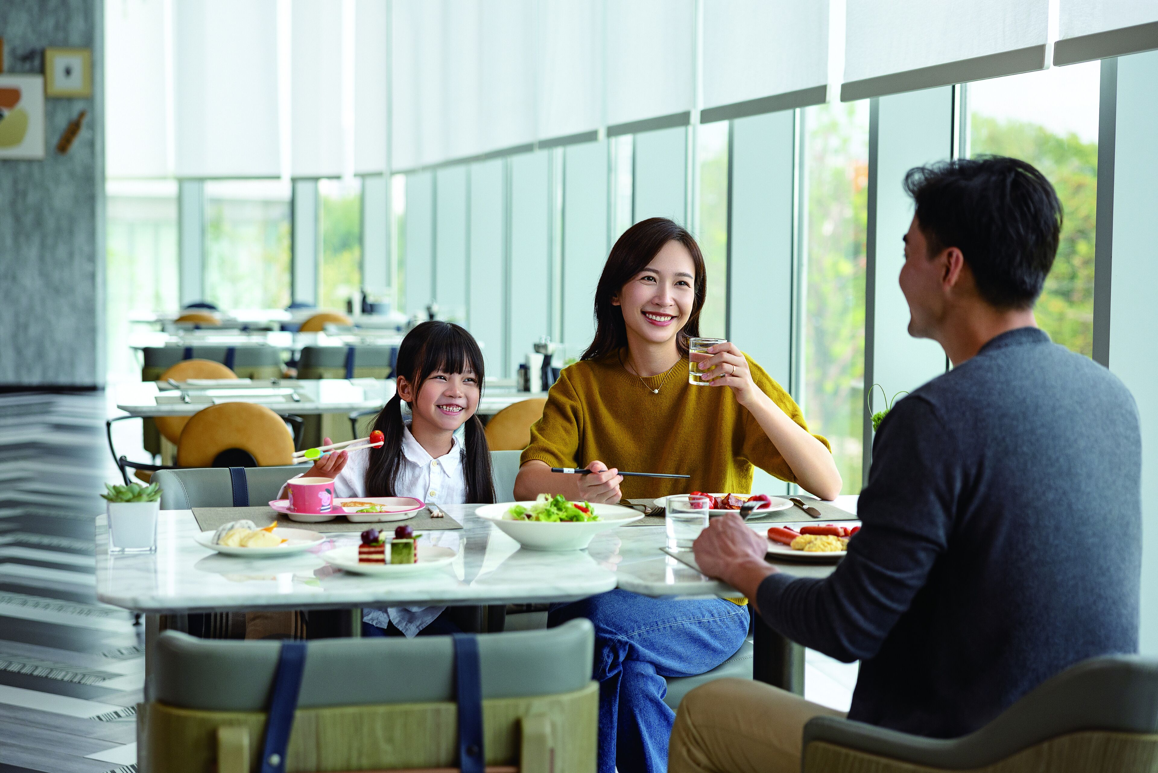 A modern dining area with large windows, tables with chairs, and various dishes.