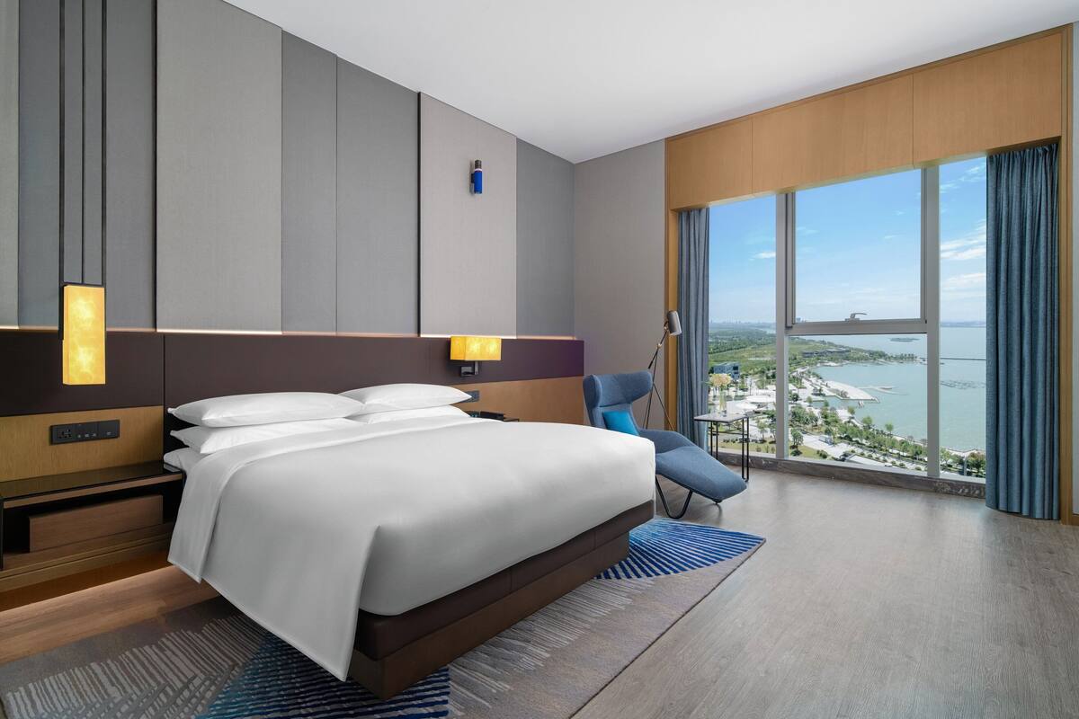 A modern hotel room with a large bed, a desk, and a view of a body of water.