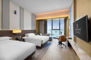 A hotel room with two beds, a desk, a chair, a television, and a large window with a view of the water. - Renaissance Changzhou Wujin Hotel (Changzhou)