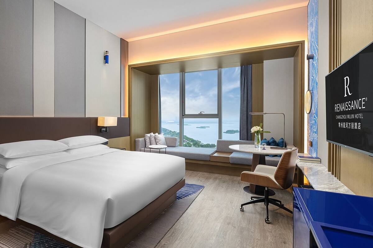 A modern hotel room with a large bed, a desk, and a view of the city.